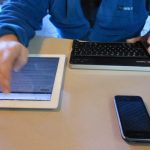 Mãos usando tablet, celular e teclado para pesquisar um carro à distância