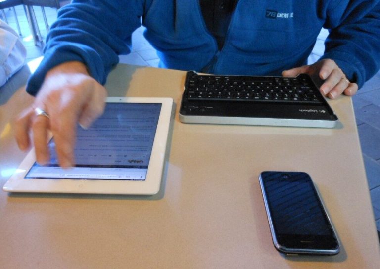 Mãos usando tablet, celular e teclado para pesquisar um carro à distância