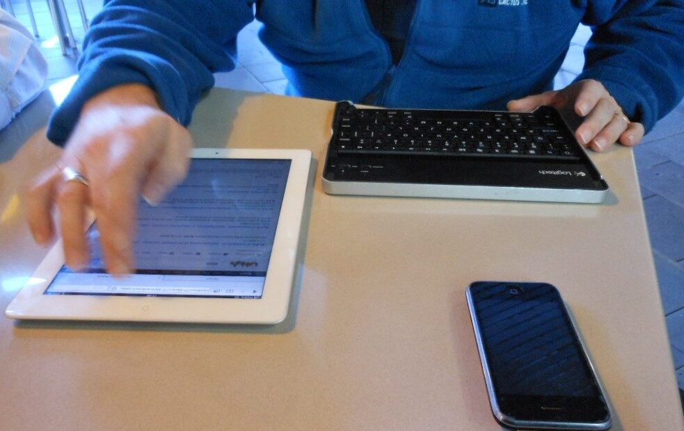 Mãos usando tablet, celular e teclado para pesquisar um carro à distância